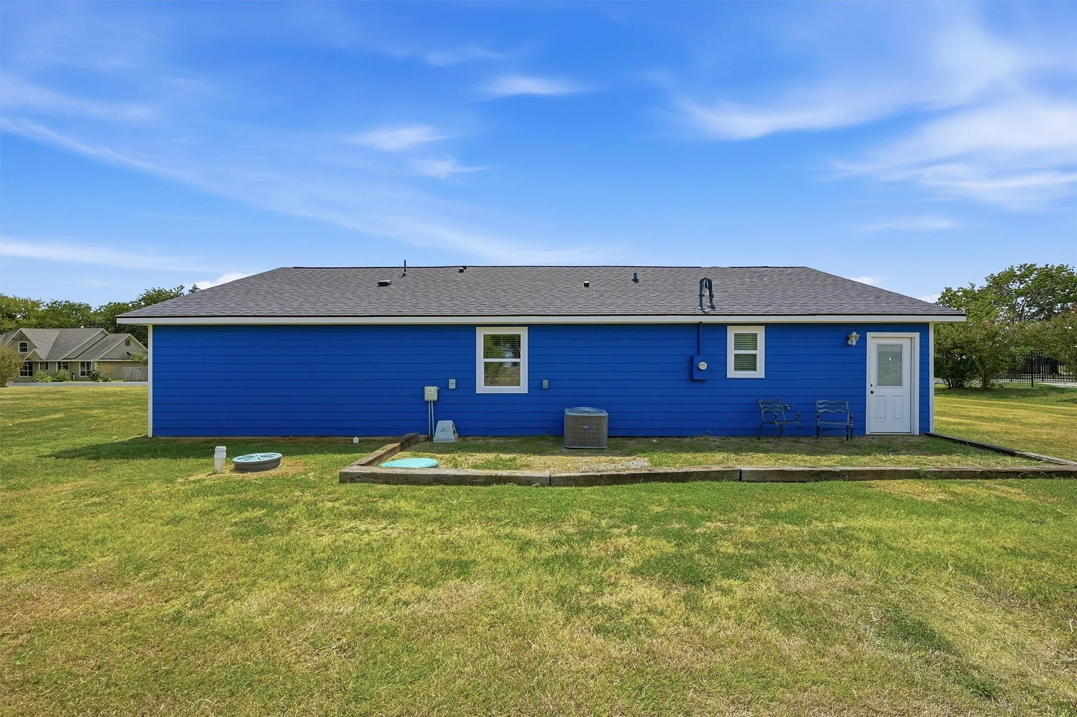 Blue exterior siding with white trim, a dark shingle roof, a white exterior door, and a single exterior window