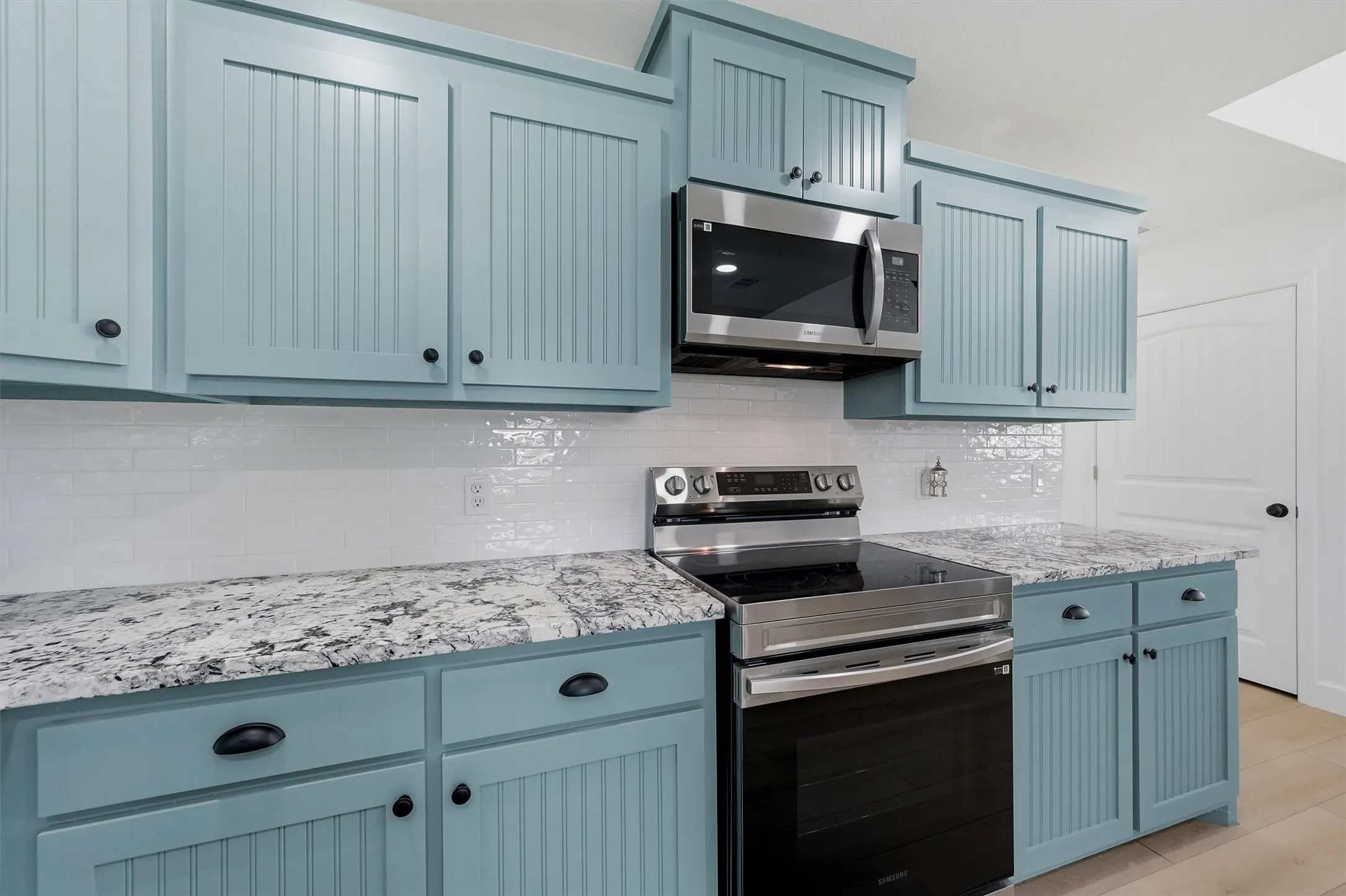 Light blue beadboard cabinetry, stainless steel appliances, white subway tile backsplash, and speckled countertops