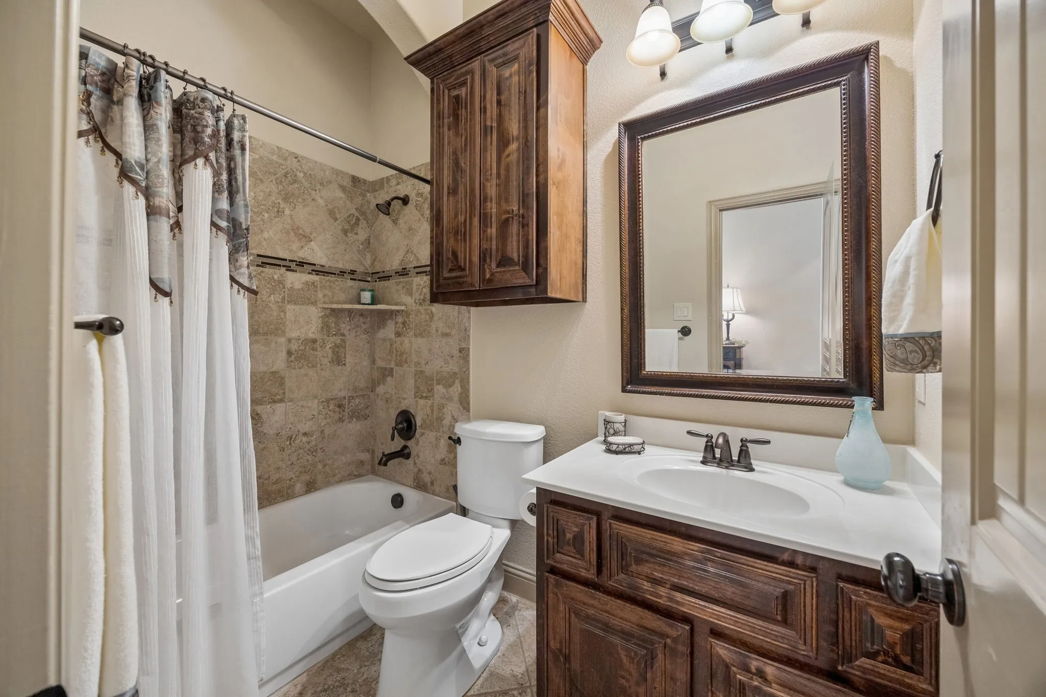 Full-size bathtub with tiled surround, wood-finish vanity with countertop, framed mirror, and built-in wood-finish cabinet