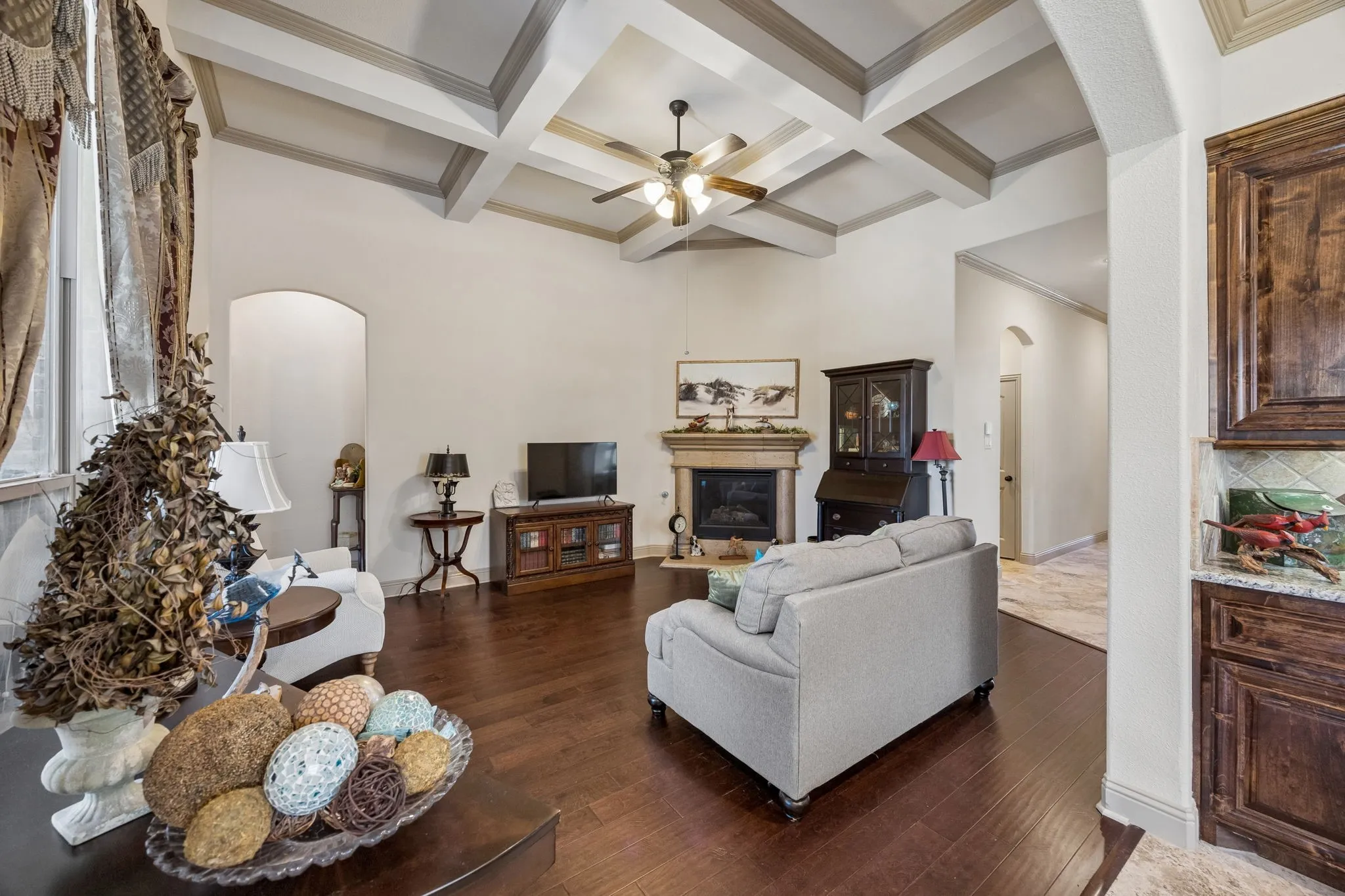 Vaulted ceiling with decorative beams, wood-finish flooring, built-in fireplace, and integrated ceiling fan