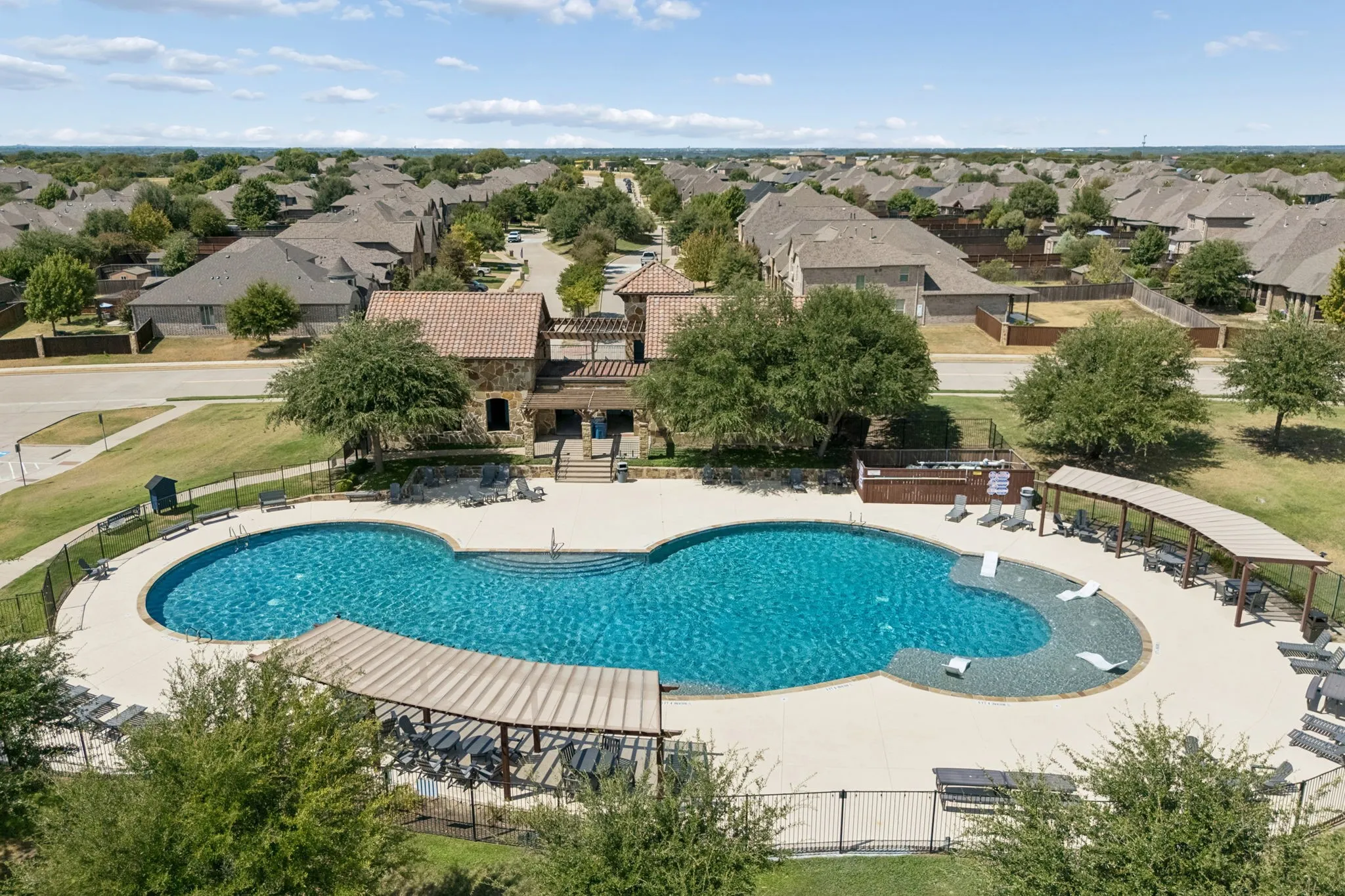 Expansive community pool with integrated tanning ledge, surrounded by concrete decking and multiple shaded lounge areas