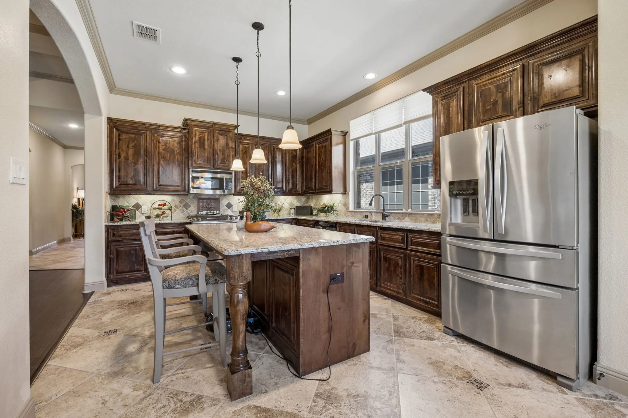 Kitchen featuring dark wood cabinetry, a granite-top island, stainless steel appliances, pendant lighting, and tiled flooring
