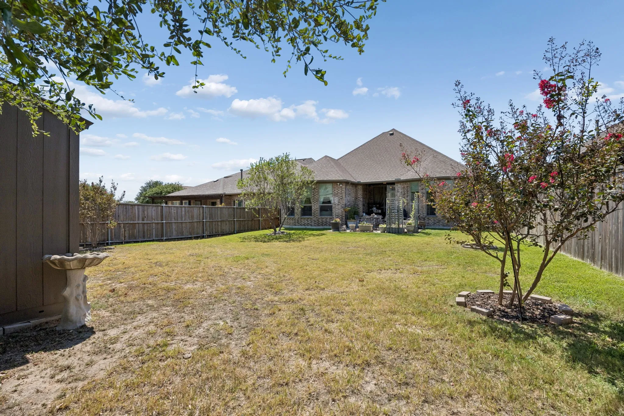 Spacious backyard featuring a wood privacy fence, mature trees, and an exterior storage shed