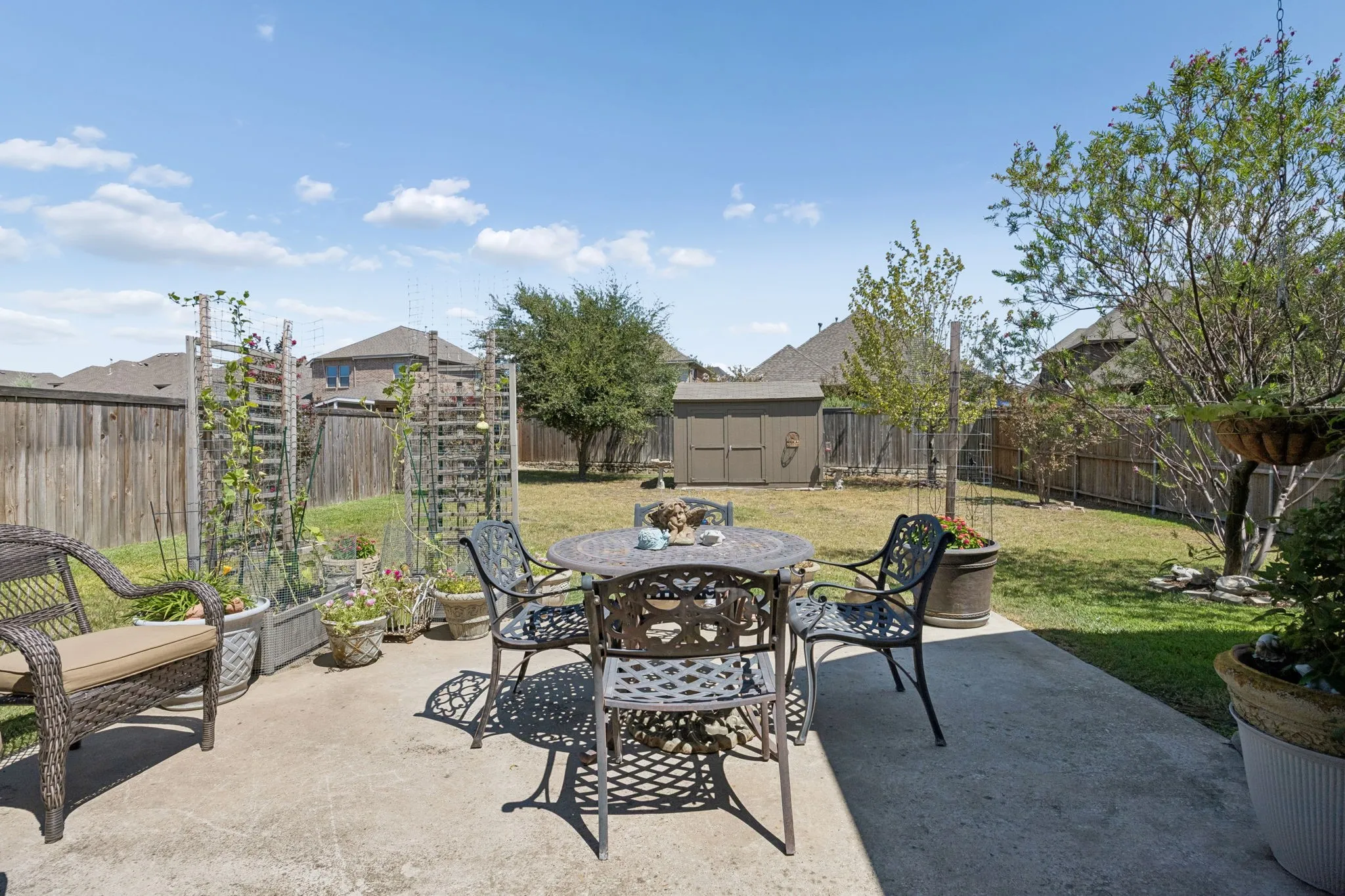 Concrete patio area with a fenced backyard, featuring a storage shed and mature trees