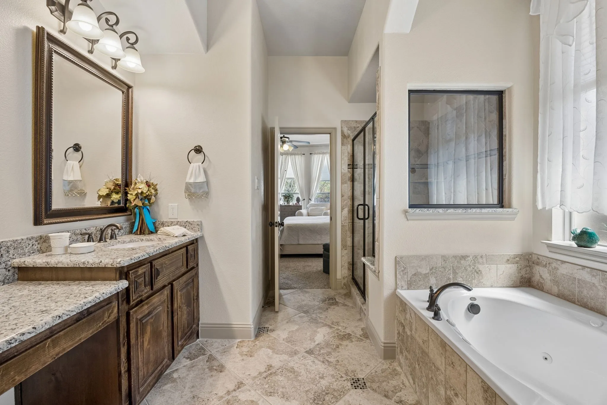Bathroom featuring an undermount sink, granite-style countertop, wood-finish cabinetry, a framed mirror, and a tiled soaking tub