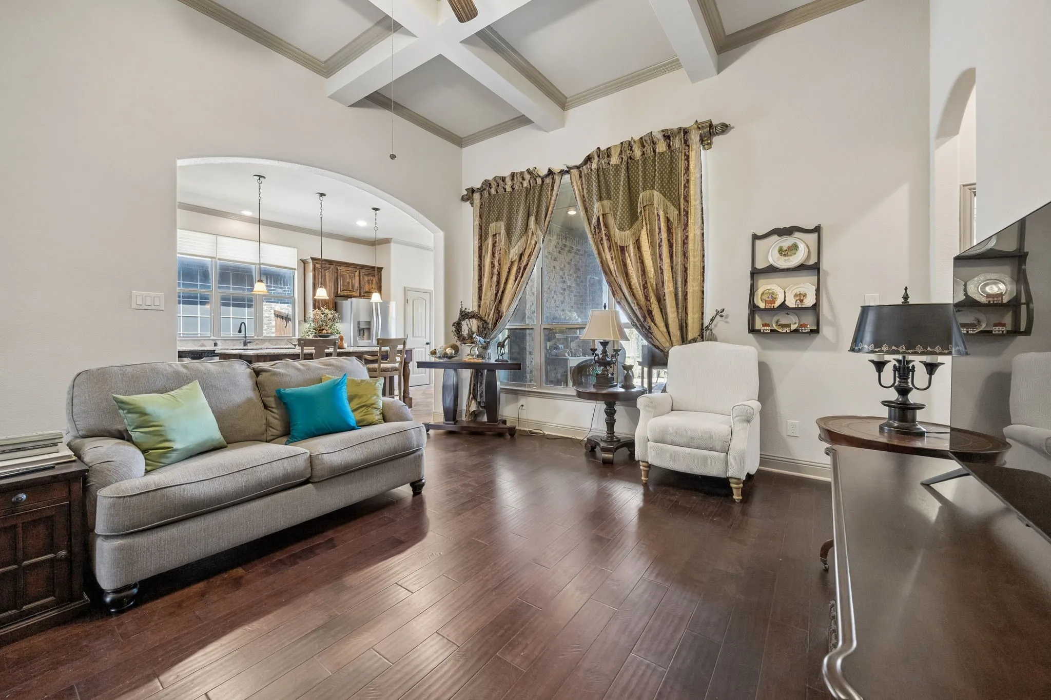 Sophisticated living room showcasing coffered ceiling details, dark wood-finish flooring, and an elegant color palette