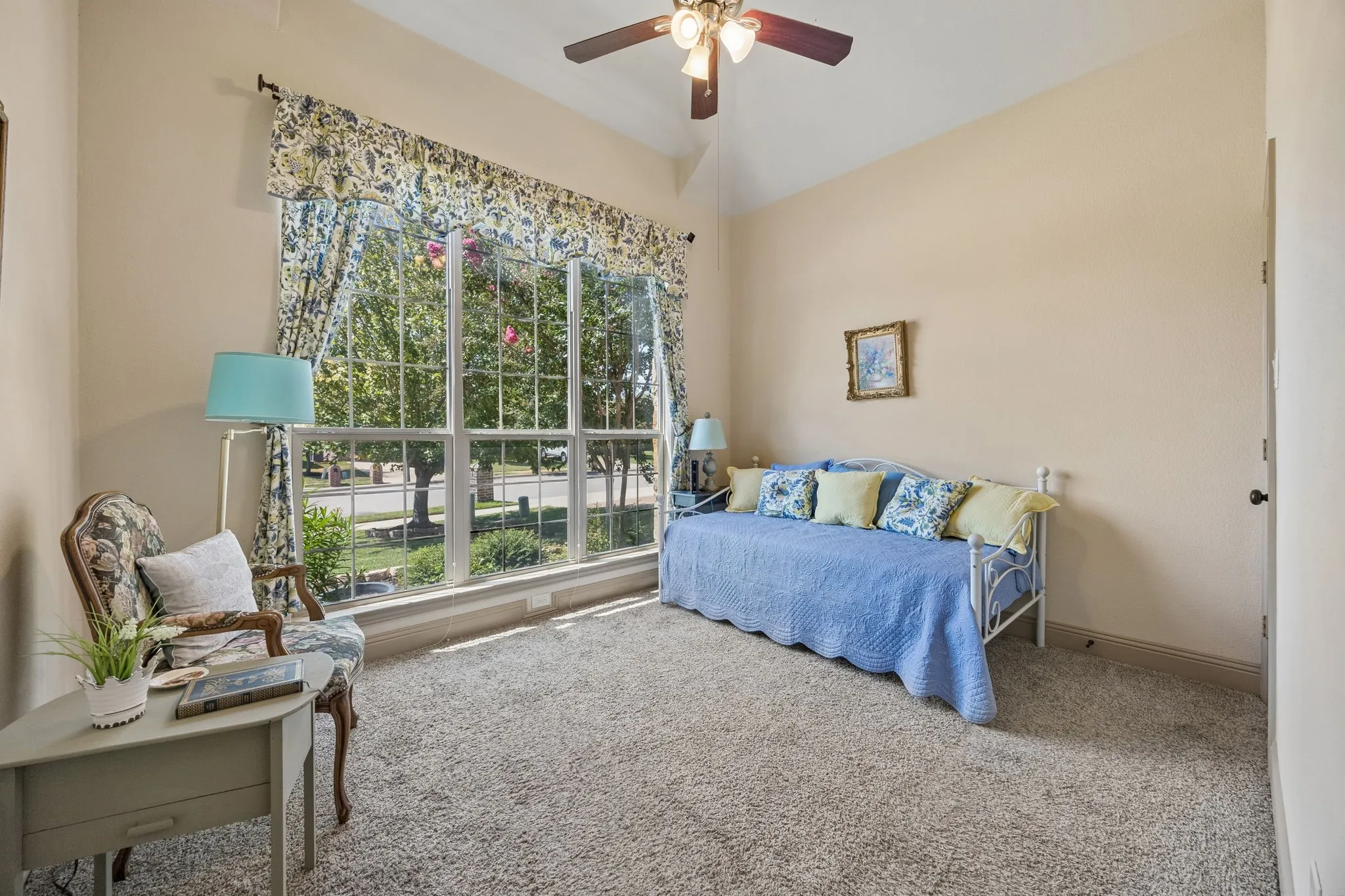 Carpeted interior space featuring a vaulted ceiling with a ceiling fan, a large window with multiple panes, and light-toned wall paint