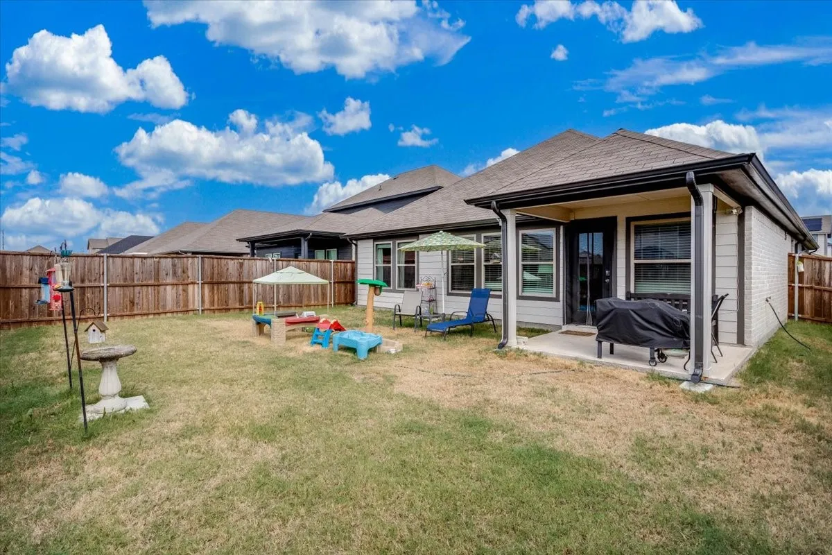 Expansive backyard featuring a privacy fence, covered patio, and a light brick exterior