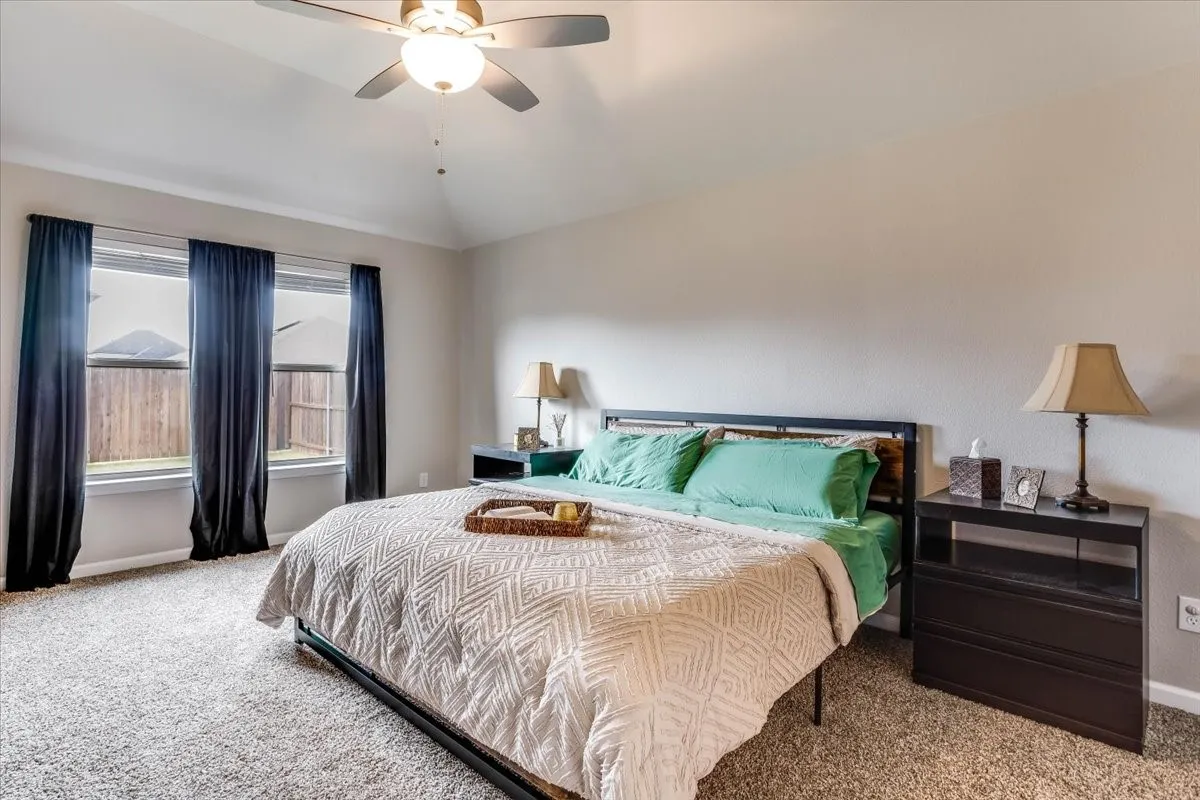 Vaulted ceiling with a ceiling fan, three windows, and plush carpet flooring