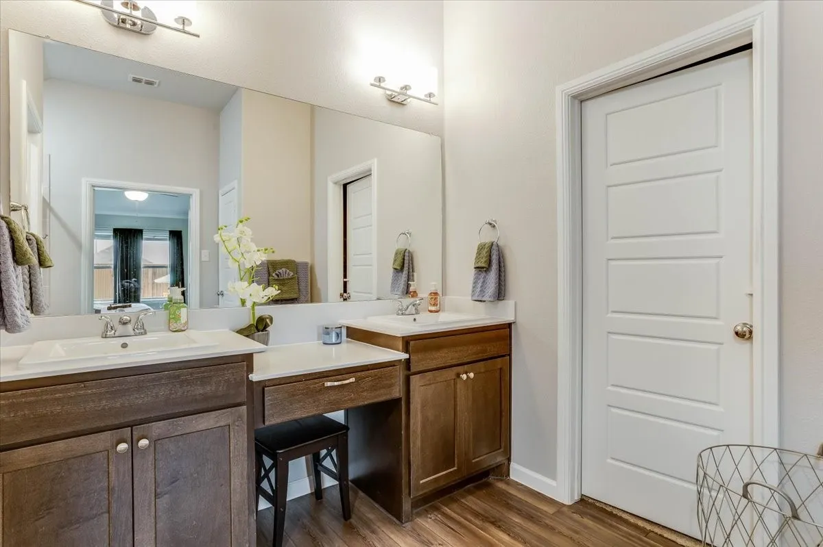 Dual vanity with wood-finish cabinetry, integrated sinks, and polished chrome fixtures