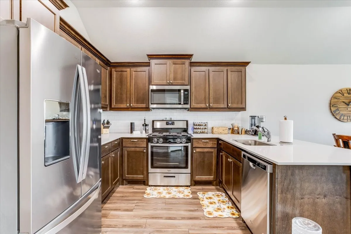 Kitchen featuring stainless steel appliances, wood-finish flooring, white subway tile backsplash, white countertops, and dark wood cabinetry
