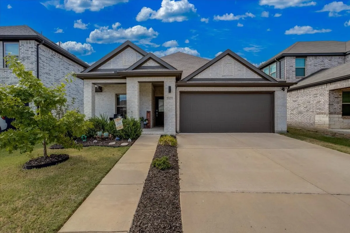 Brick exterior with stone accents, covered entry, attached two-car garage, concrete driveway, and established landscaping