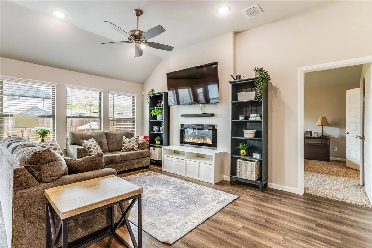 Vaulted ceiling with recessed lighting, wood-finish flooring, multiple windows with blinds, and a built-in electric fireplace