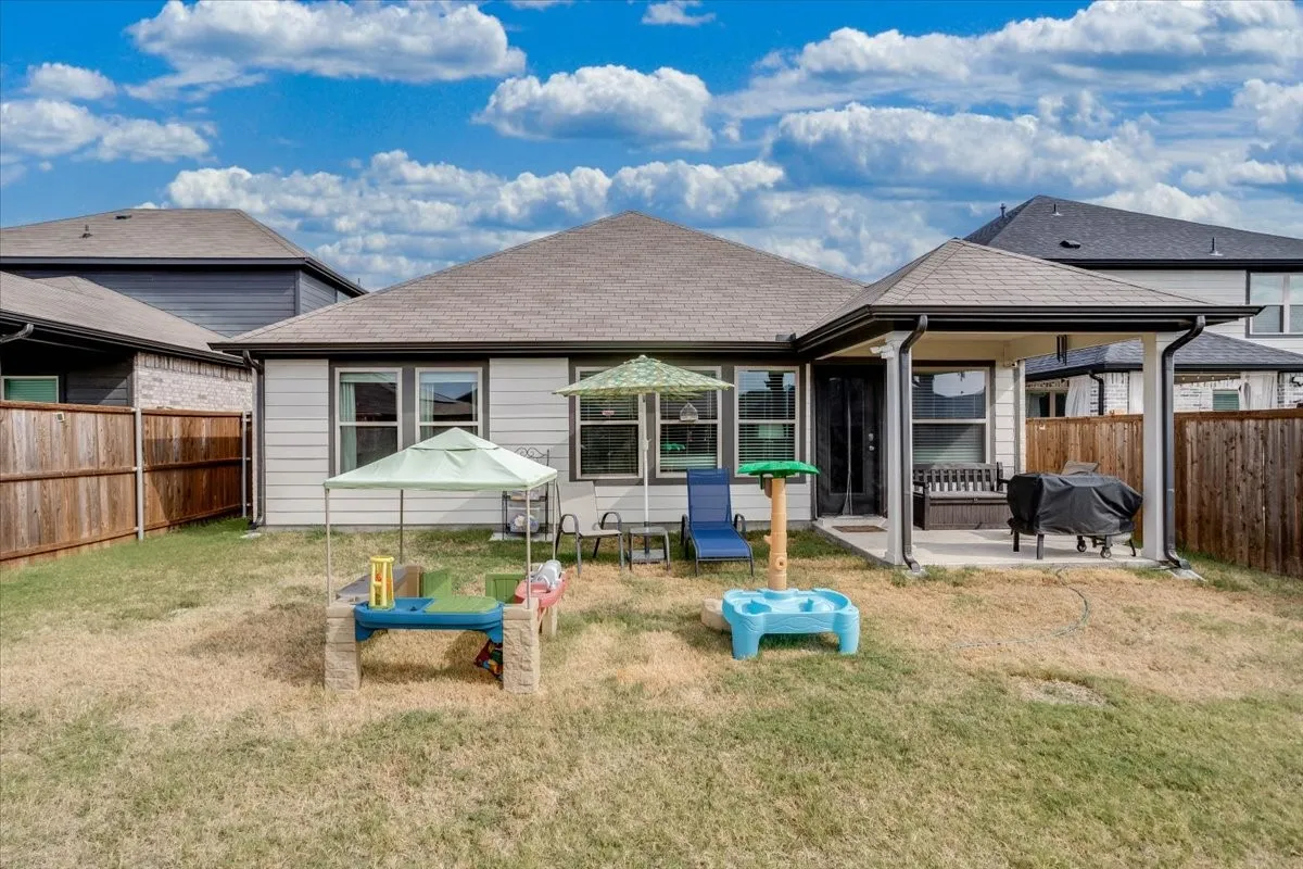 Expansive backyard featuring a covered patio, privacy fencing, and a light-colored exterior with multiple windows