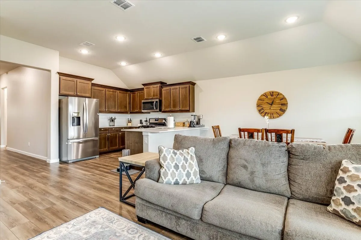 Open-concept living space with wood-finish flooring, vaulted ceilings, and recessed lighting