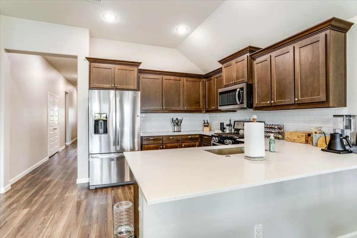 Kitchen featuring rich wood cabinetry, stainless steel appliances, white subway tile backsplash, white countertops, and wood-finish flooring