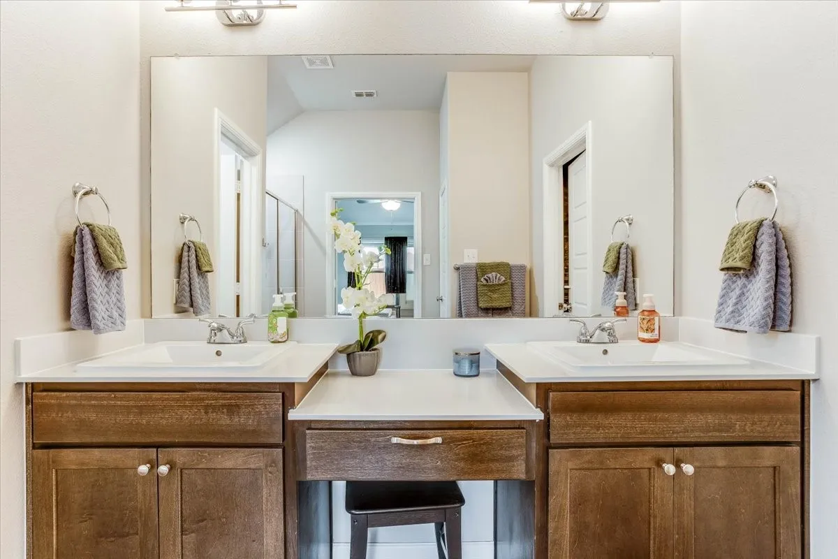 Dual undermount sinks with chrome fixtures, white countertops, wood-finish cabinetry, and an integrated vanity area