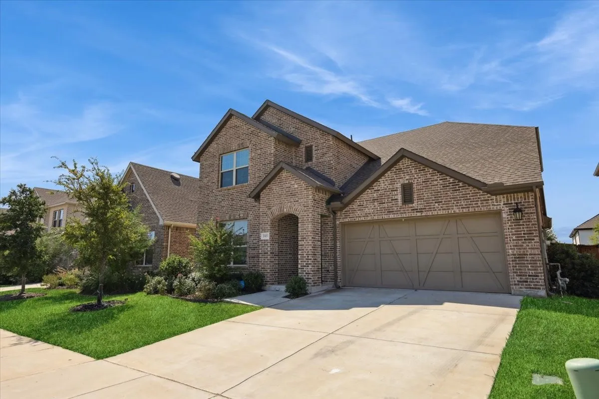 View of front facade featuring brick siding, concrete driveway, a front yard, an attached garage, and roof with shingles