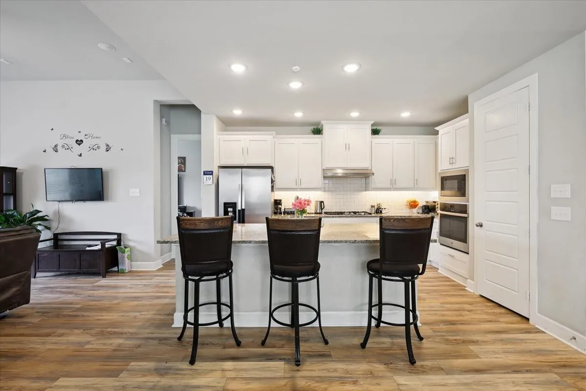 Kitchen featuring white cabinets, tasteful backsplash, stainless steel appliances, light stone countertops, and light wood-style flooring
