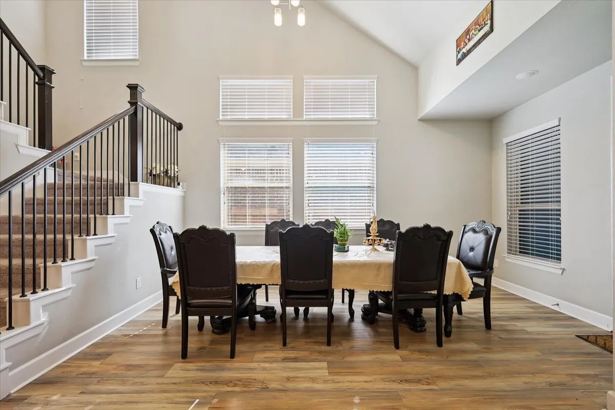 Dining space with high vaulted ceiling, light wood finished floors, and stairs