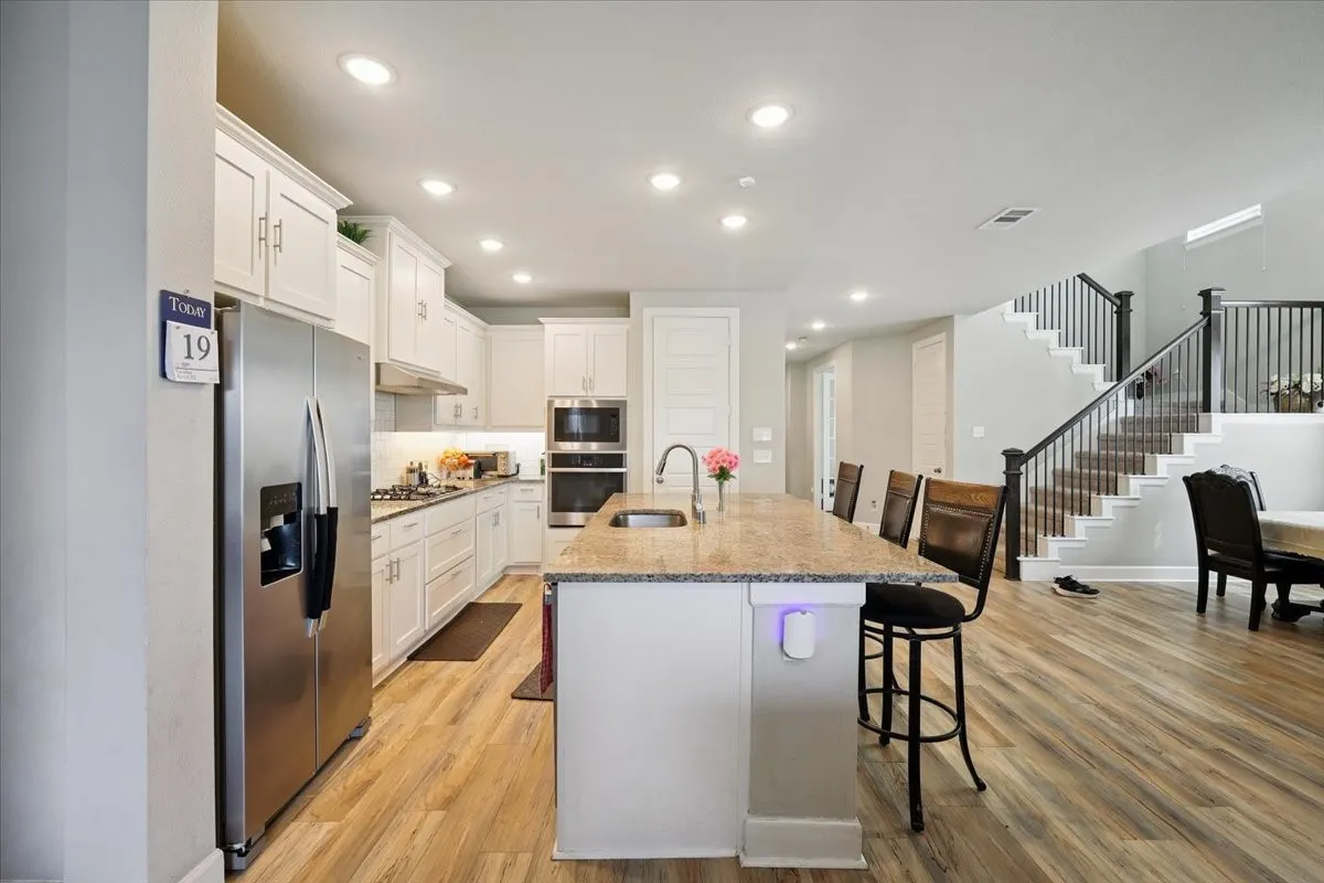 Kitchen featuring a breakfast bar area, stainless steel appliances, white cabinets, light stone countertops, and recessed lighting