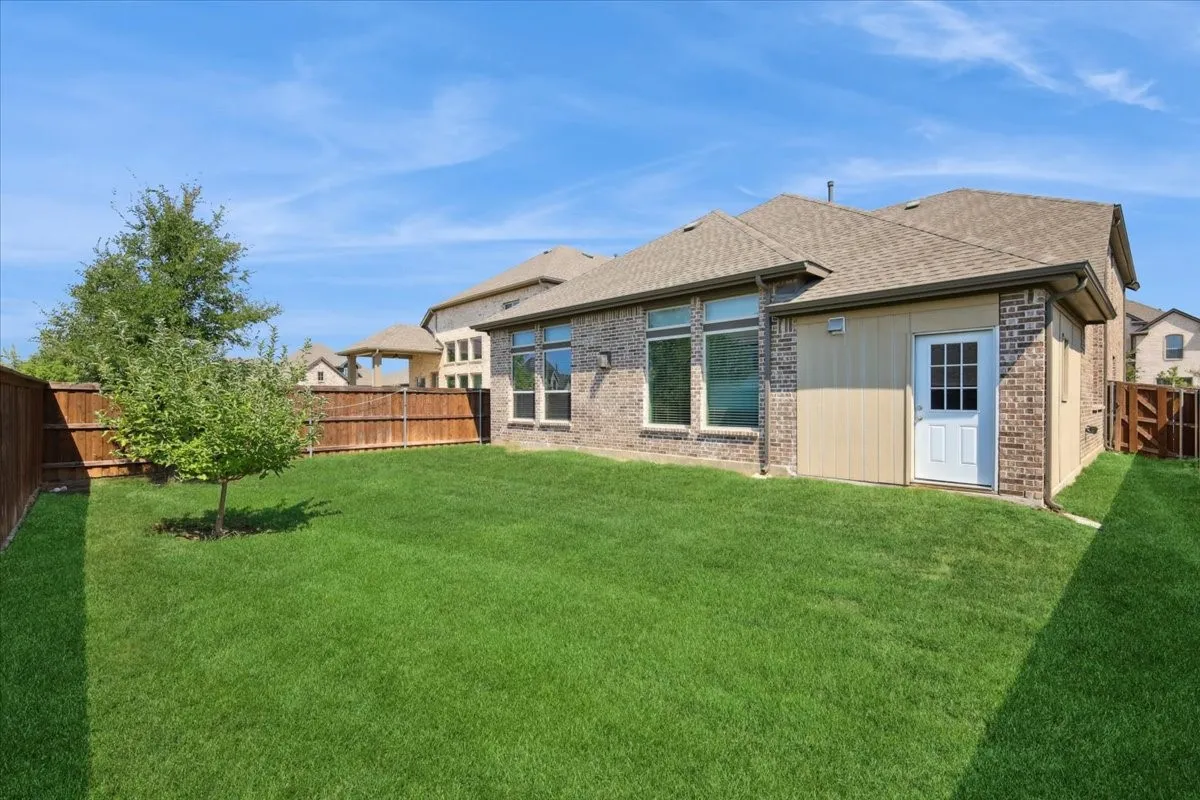 Rear view of property featuring a fenced backyard, roof with shingles, and brick siding