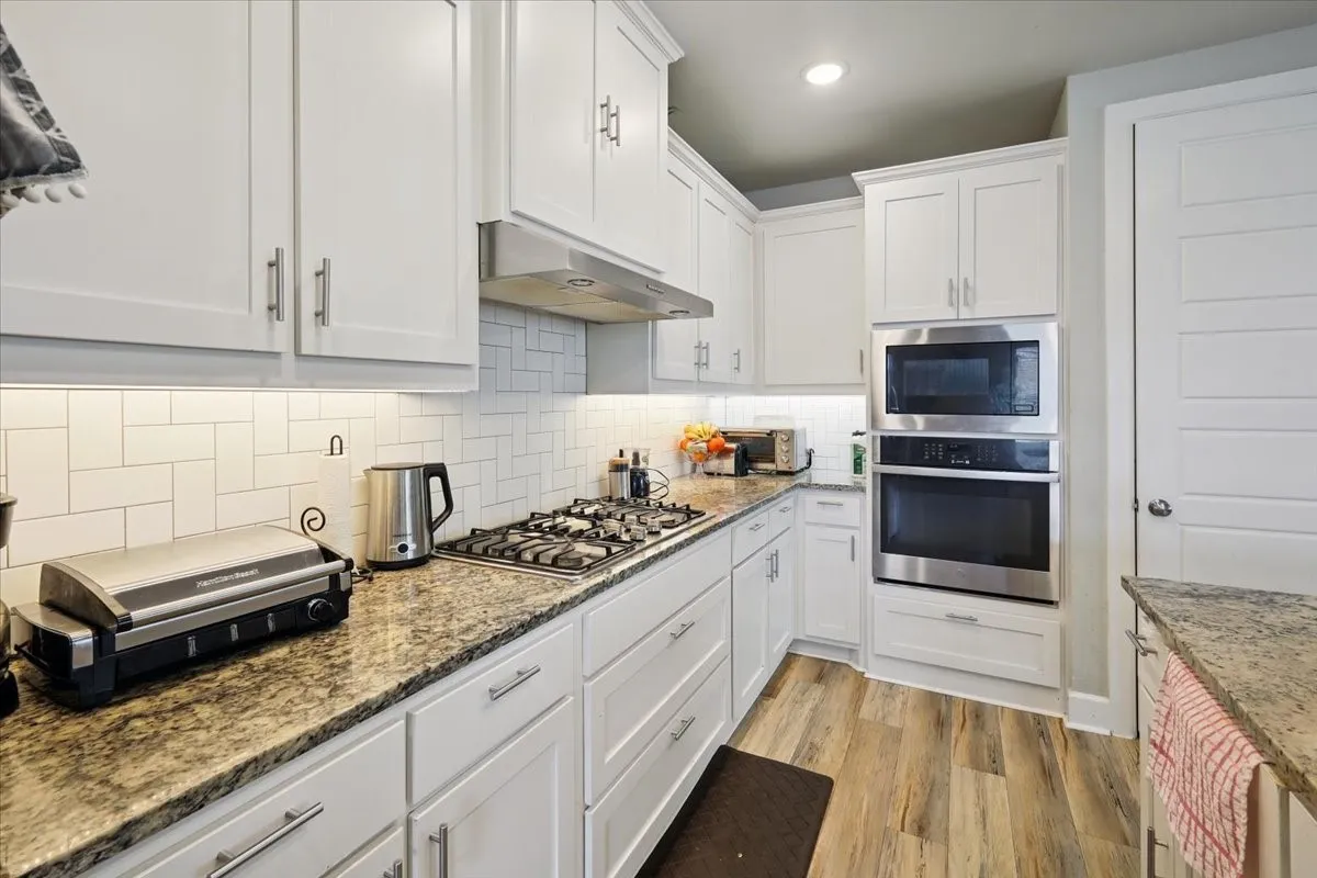 Kitchen featuring white cabinets, appliances with stainless steel finishes, backsplash, light wood finished floors, and light stone countertops
