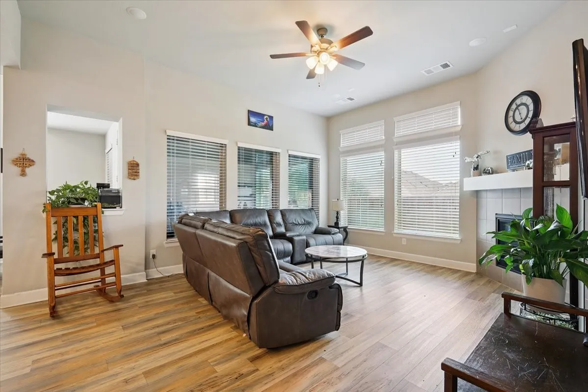 Living area with light wood finished floors, a tile fireplace, and a ceiling fan
