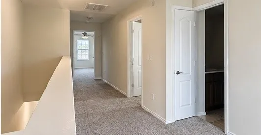 Carpeted hallway with white trim, paneled doors, and ceiling fan