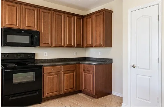 Wood-finish cabinetry, black countertop, black range, and built-in microwave