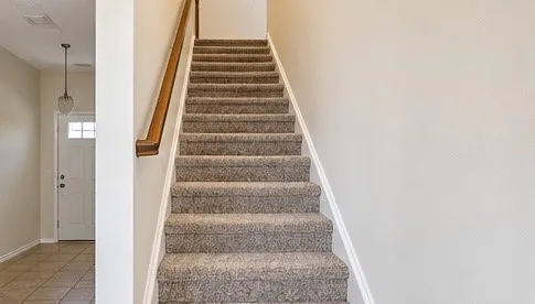 Carpeted staircase with a wood handrail, tile flooring, and a white front door with lites