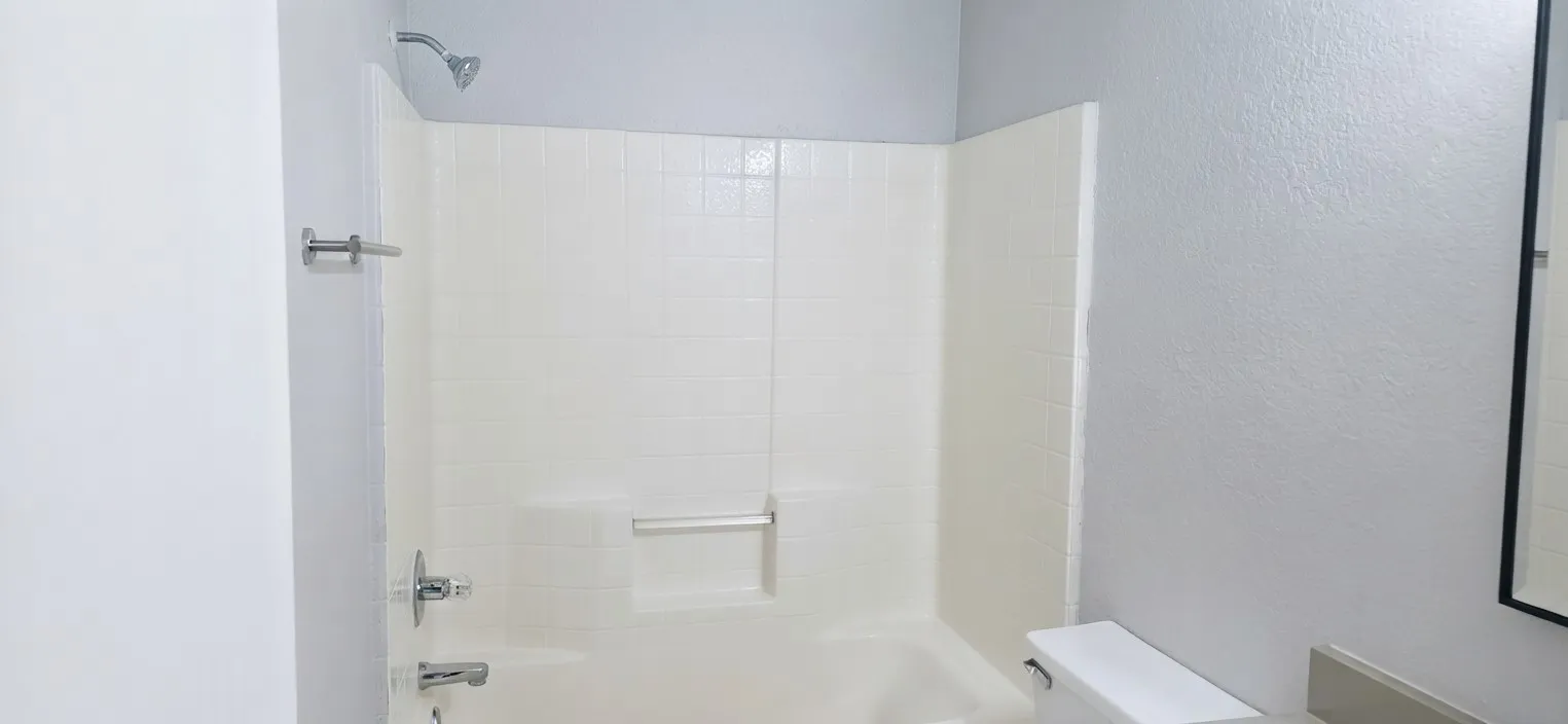 Bathtub with integrated tile surround, chrome shower fixtures, and a wall-mounted grab bar