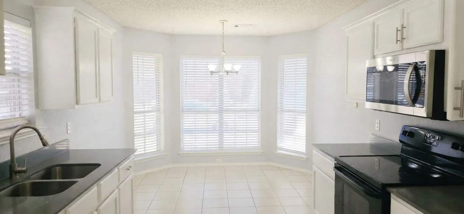 Kitchen featuring white cabinetry, dark countertops, a double basin sink, stainless steel microwave, and white tile flooring