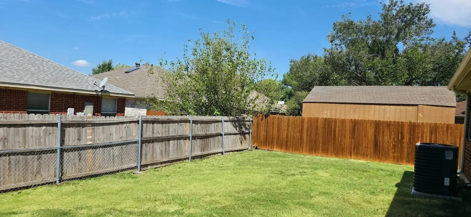 Expansive backyard with a manicured lawn, wood fencing, and a detached storage shed