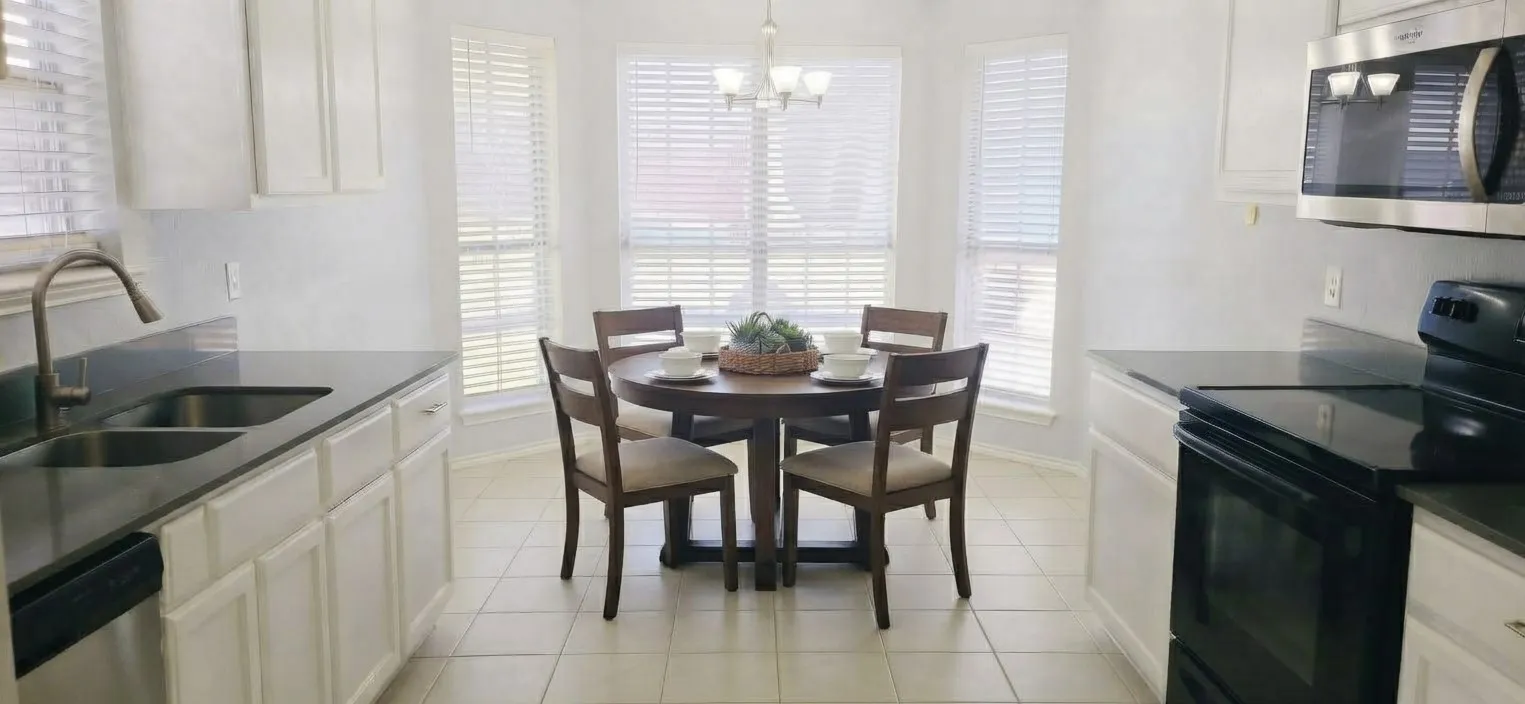 White cabinetry, dark countertops, built-in microwave, tile flooring, and a bay window