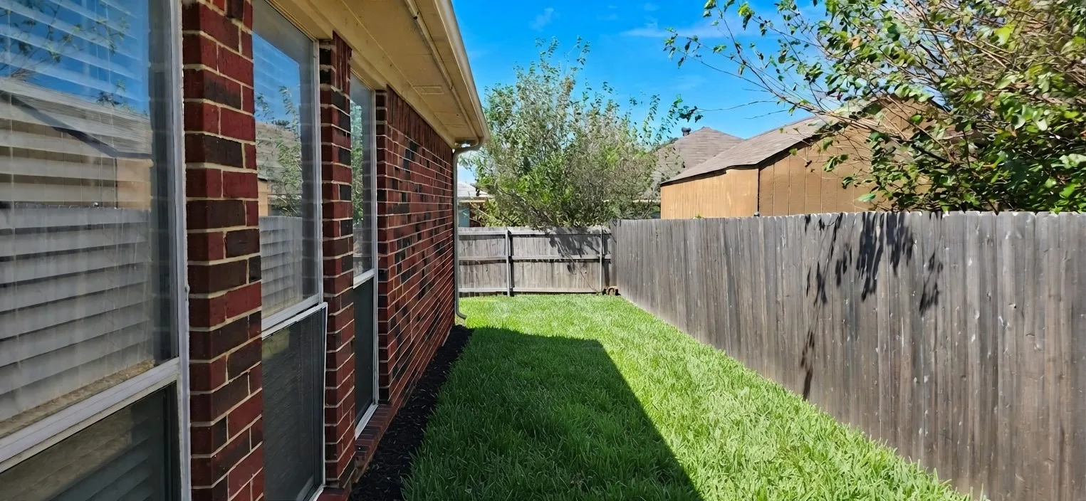 Brick exterior with multiple windows, leading to a private fenced yard with a manicured lawn