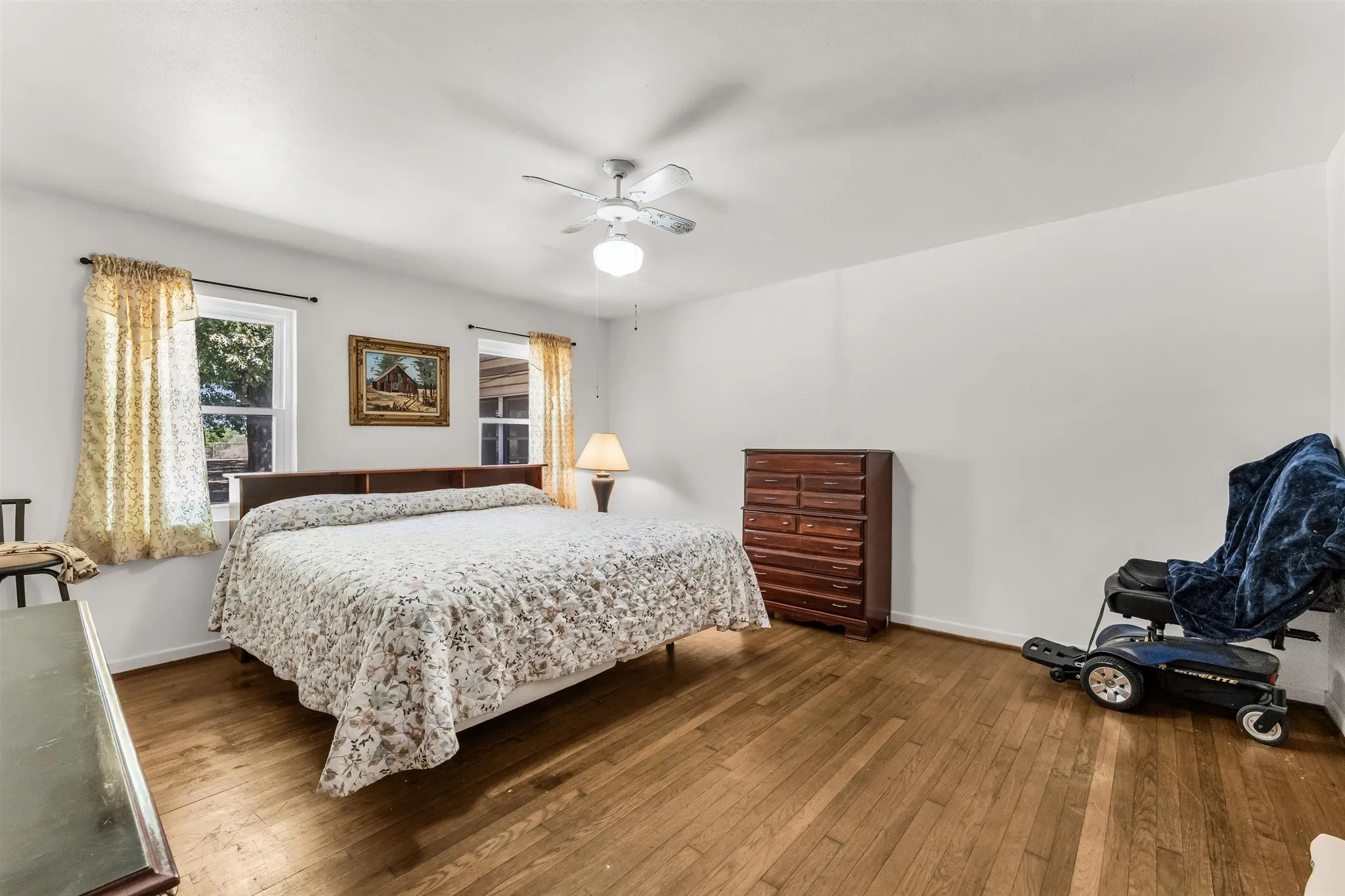 Hardwood flooring, white walls, two window units, and a ceiling fan with integrated lighting