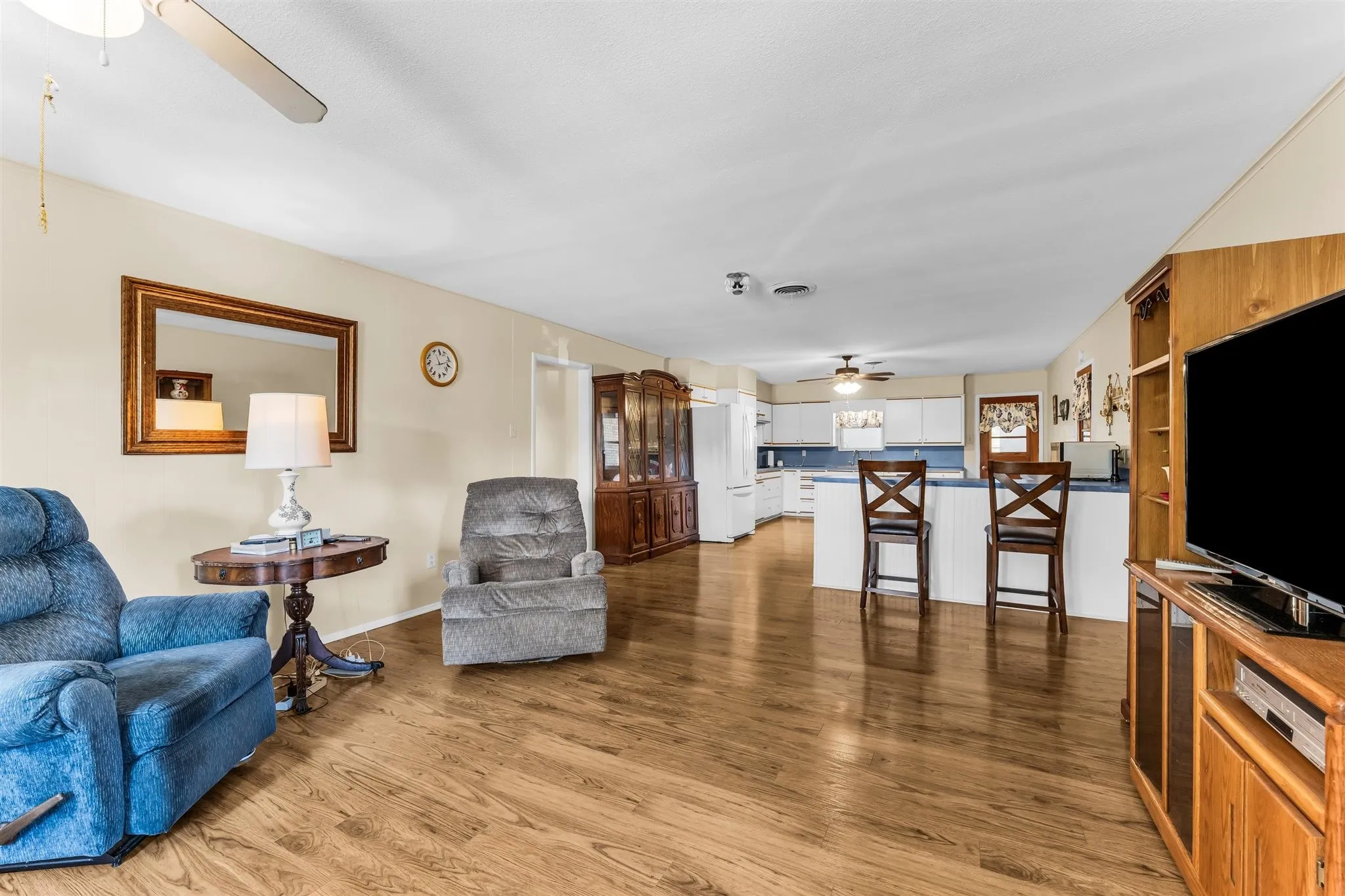 Open-concept living area featuring wood-finish flooring, a ceiling fan, and white kitchen cabinetry with a breakfast bar