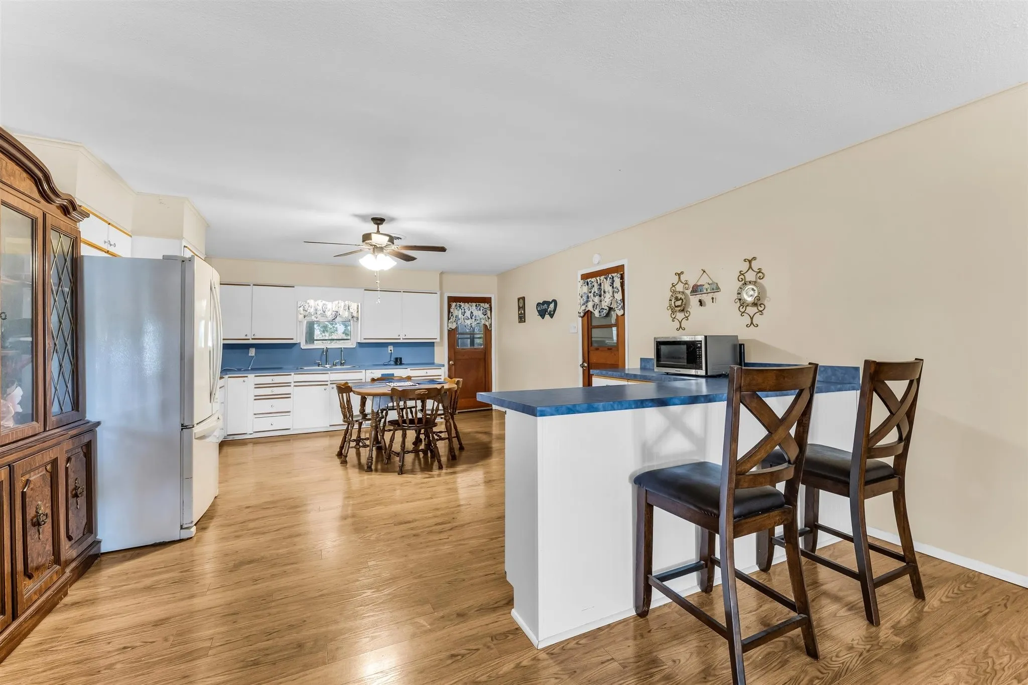 Open-concept kitchen and dining area featuring wood-finish flooring, white cabinetry, a built-in breakfast bar, and stainless steel refrigerator