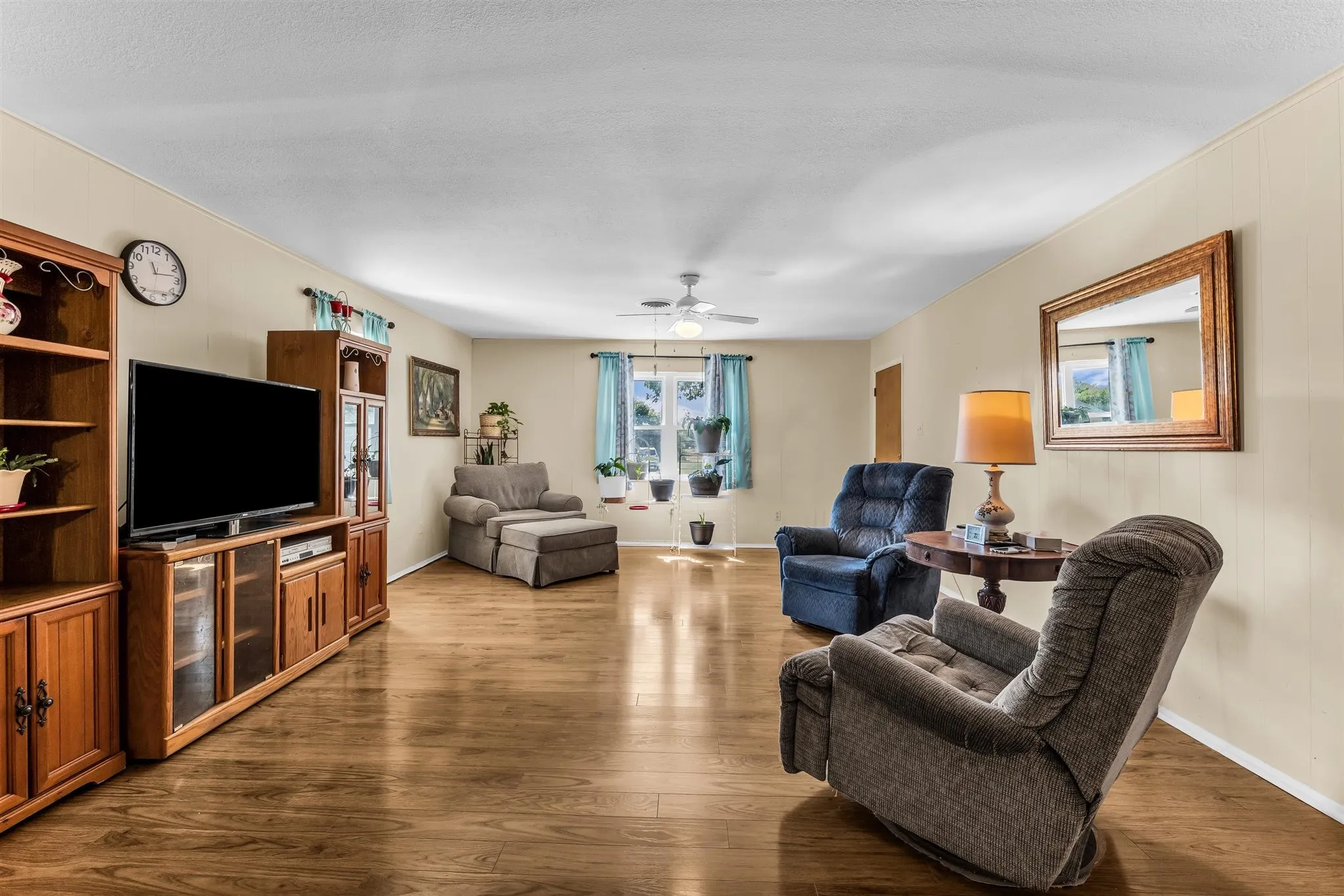 Spacious living area featuring wood-finish flooring, light-toned walls, and a ceiling fan