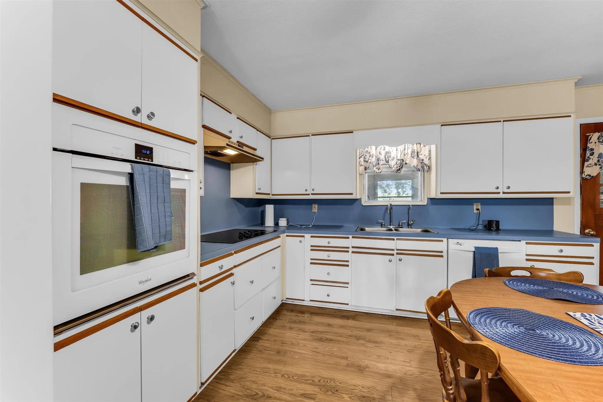 White cabinetry with wood-finish trim, blue countertops, built-in wall oven, and wood-finish flooring