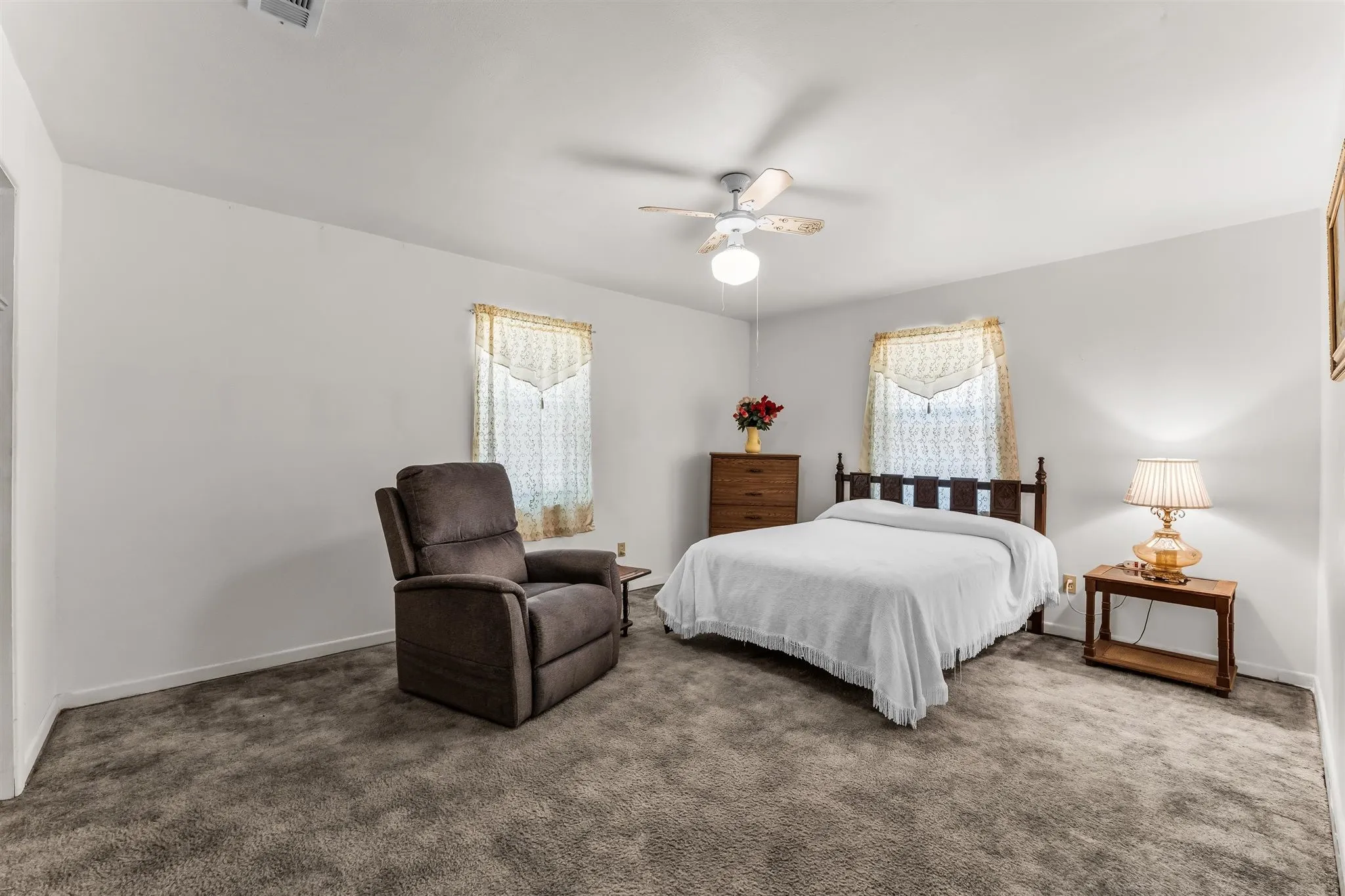 Carpeted bedroom featuring a ceiling fan with integrated lighting and two windows