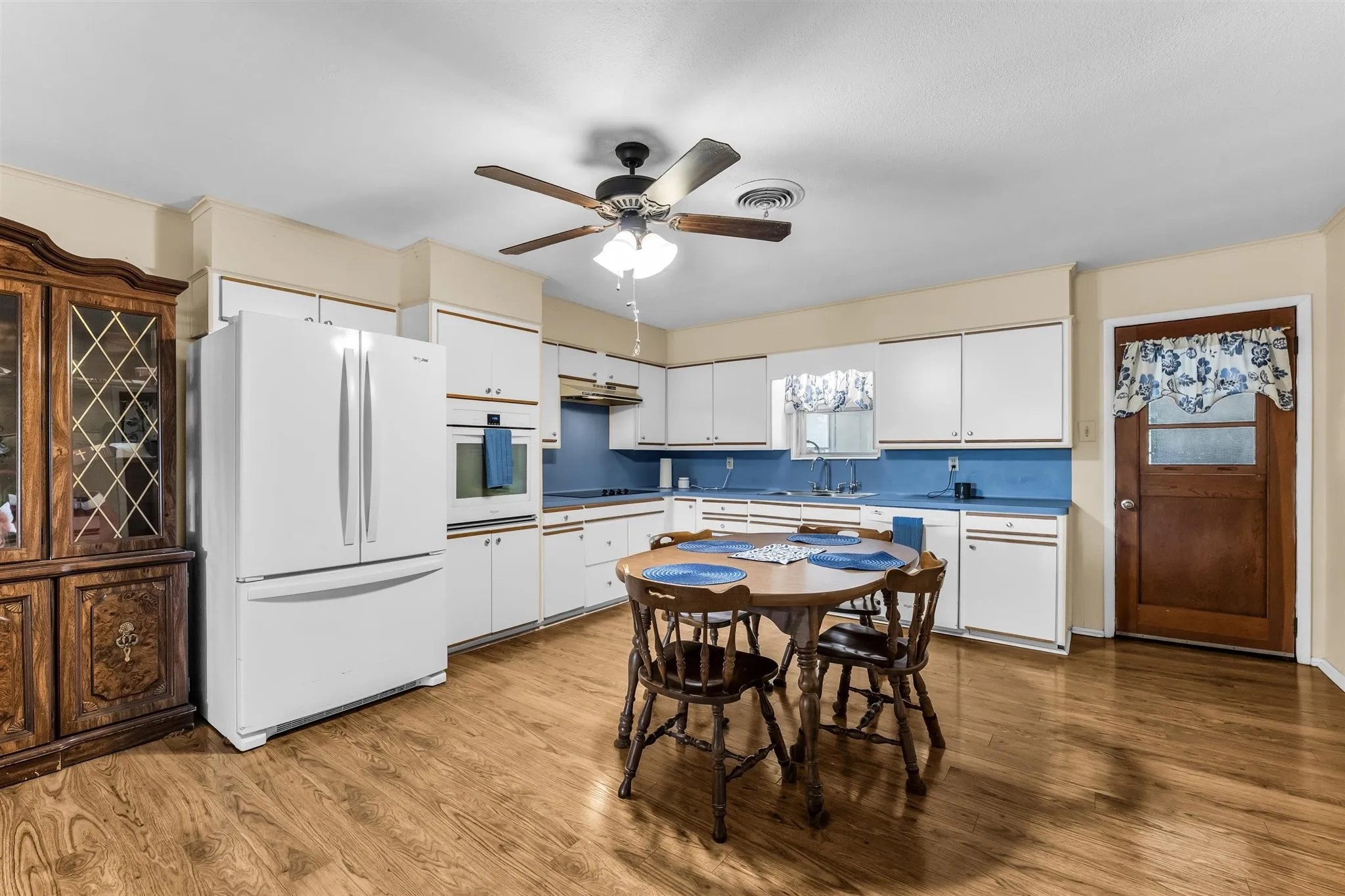 Kitchen featuring wood-finish flooring, white cabinetry, integrated white appliances, and a ceiling fan