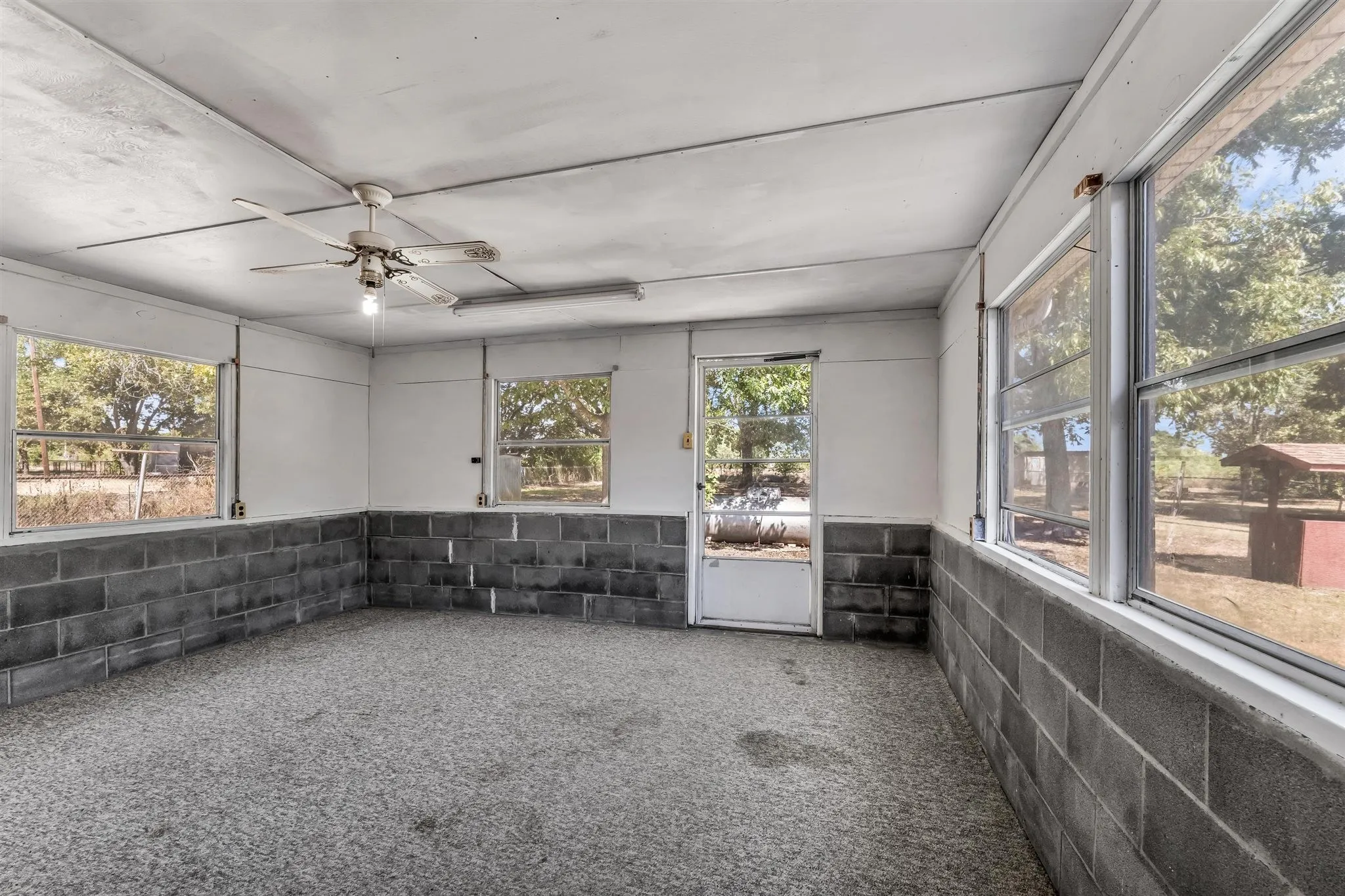 Room featuring multiple windows, exposed block wall, and a ceiling fan