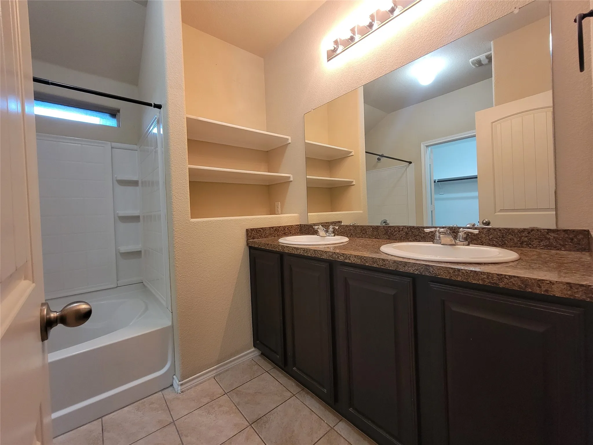Dual undermount sinks with a speckled countertop, dark wood-finish cabinetry, and a large wall-mounted mirror