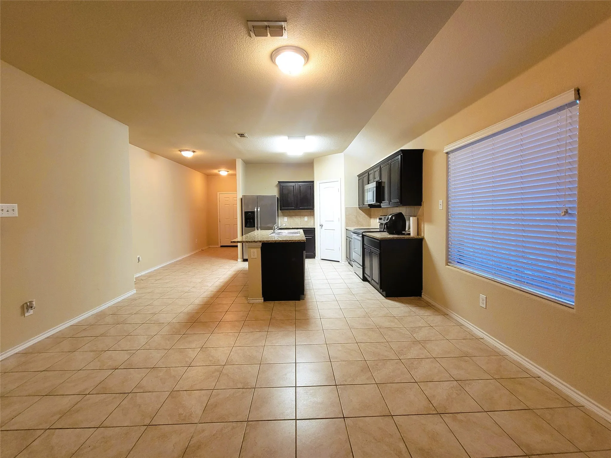 Open-concept kitchen and living area featuring tile flooring, dark wood cabinetry, and stainless steel appliances