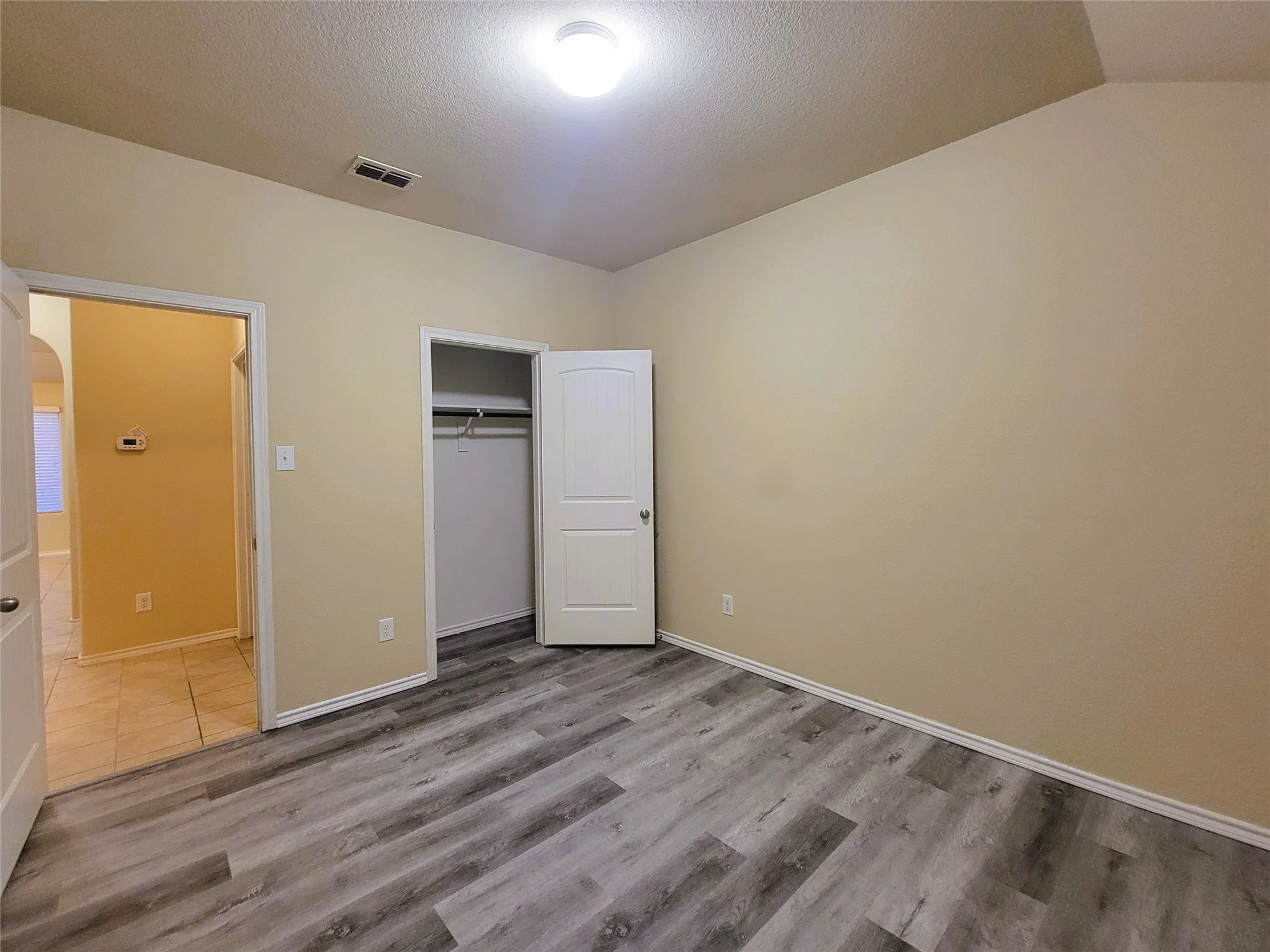 Wood-finish flooring throughout, light-toned wall paint, white trim, and a built-in closet with a two-panel door