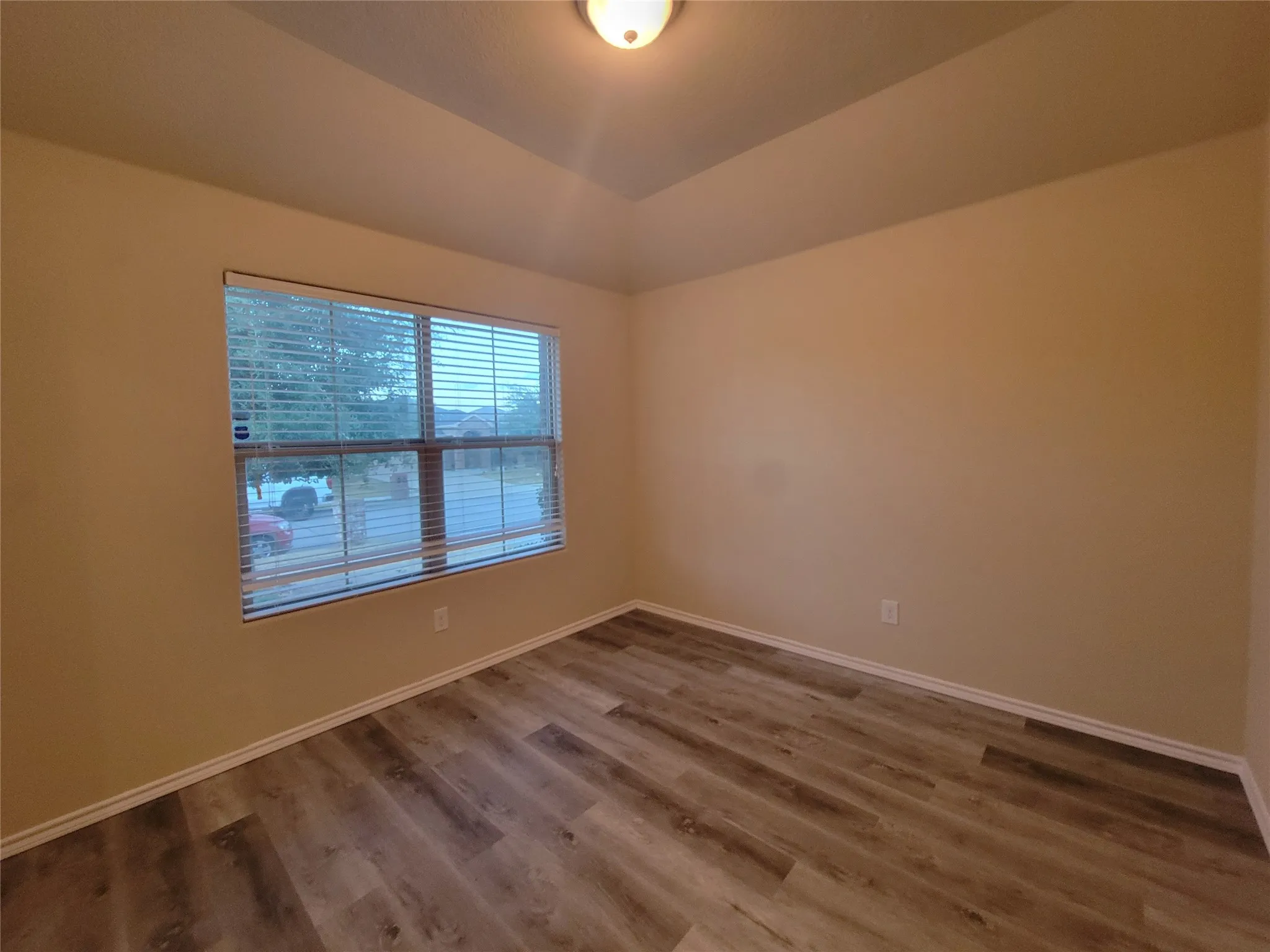 Vinyl Plank Wood-finish flooring, neutral wall tones, window with horizontal blinds, and a tray ceiling with a flush-mount light fixture