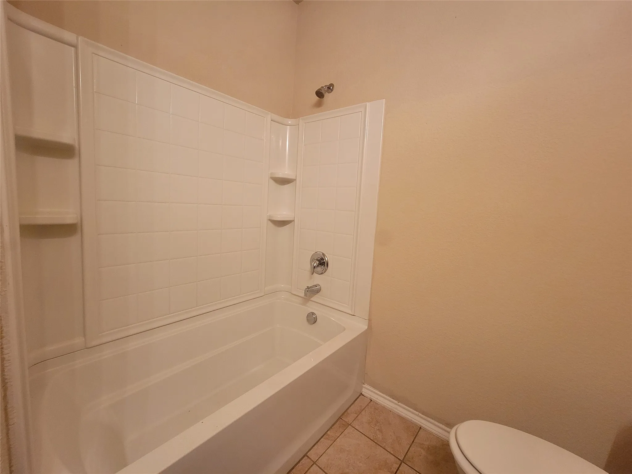 Built-in bathtub with integrated shelving, chrome fixtures, and tiled flooring