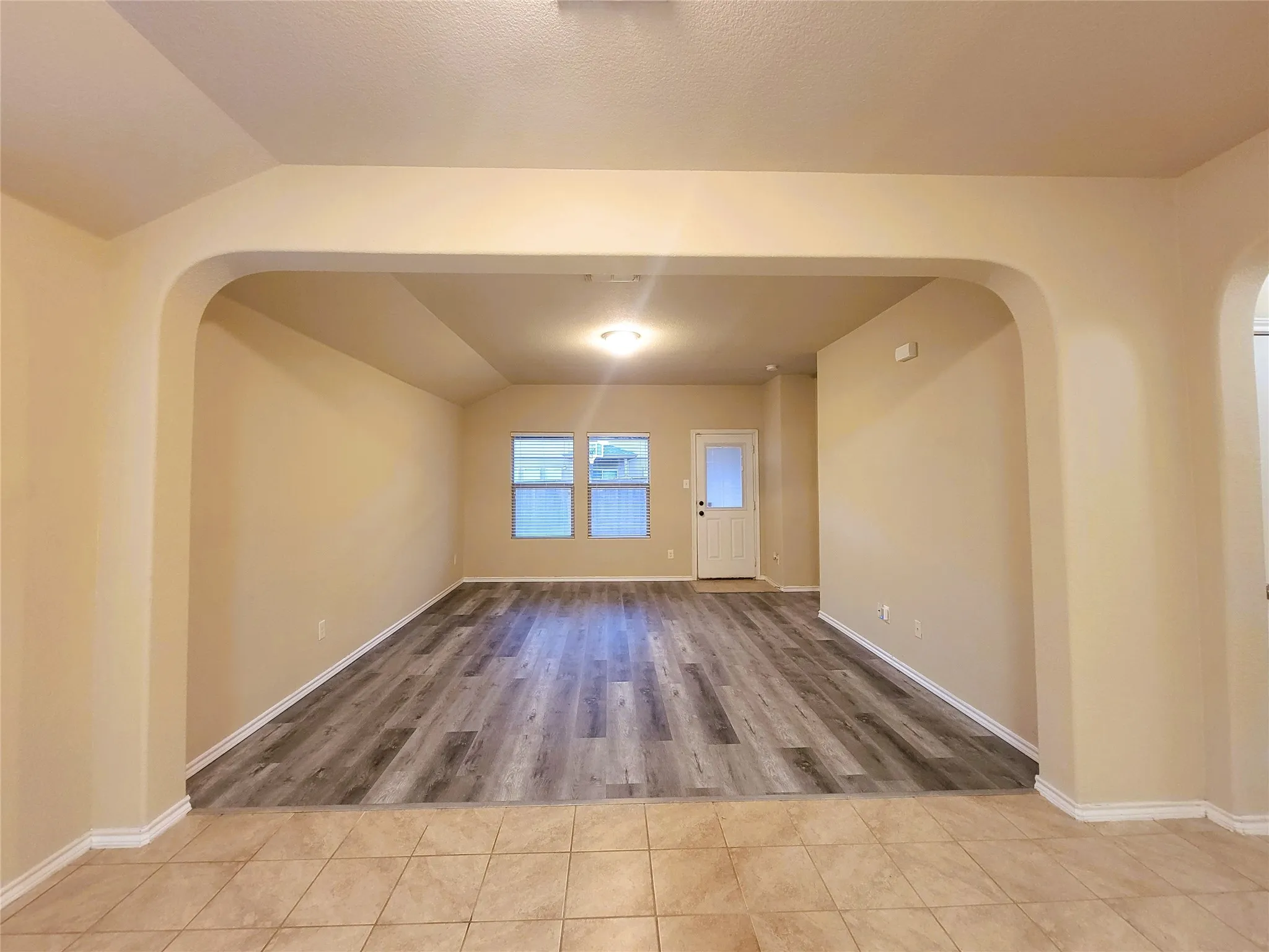 Open-concept room featuring wood-finish flooring, recessed lighting, arched doorways, and multiple windows providing natural light